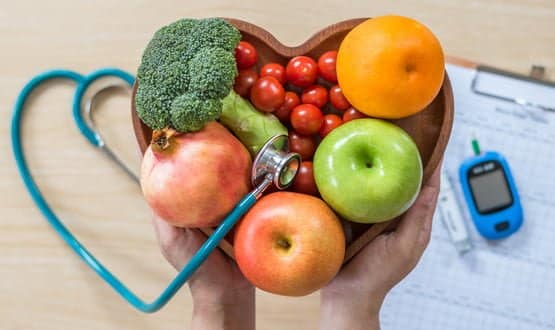 A person holds a bowl containing fruit and vegetables