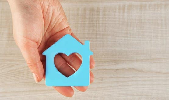 A hand holding a house stencil with a heart in the middle