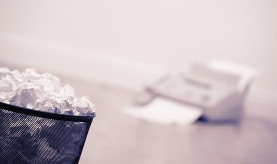 A fax machine sits behind a waste paper bin filled with crumpled paper