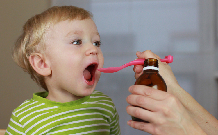 A young boy in a green striped shirt being fed medicine with a spoon