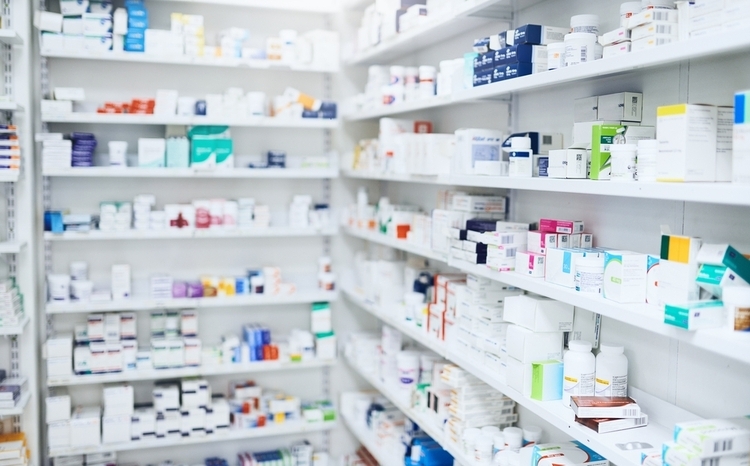 A photo of white pharmacy shelves showing rows of assorted medications in various colours and forms