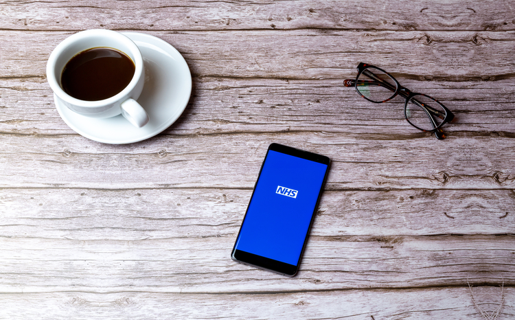 Cup of coffee, glasses and mobile phone showing the NHS App